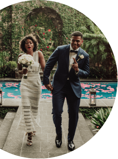 photo of a couple dancing as they walk down a paved path in a garden setting; behind them is a reflecting pool scattered with flower petals